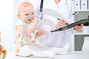 Pediatrician is taking care of baby in hospital. Little girl is being examine by doctor with stethoscope. Health care