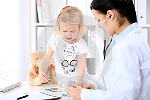 Pediatrician is taking care of baby in hospital. Little girl is being examine by doctor with stethoscope. Health care