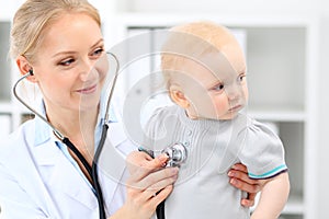 Pediatrician is taking care of baby in hospital. Little girl is being examine by doctor with stethoscope. Health care