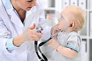 Pediatrician is taking care of baby in hospital. Little girl is being examine by doctor with stethoscope. Health care