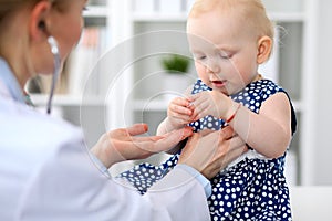 Pediatrician is taking care of baby in hospital. Little girl is being examine by doctor with stethoscope. Health care