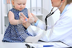 Pediatrician is taking care of baby in hospital. Little girl is being examine by doctor with stethoscope. Health care