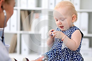 Pediatrician is taking care of baby in hospital. Little girl is being examine by doctor with stethoscope. Health care