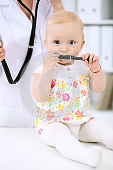 Pediatrician is taking care of baby in hospital. Little girl is being examine by doctor with stethoscope. Health care