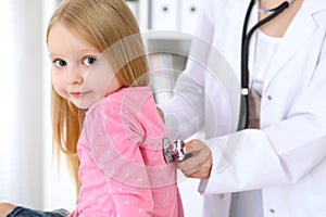 Pediatrician is taking care of baby in hospital. Little girl is being examine by doctor by stethoscope. Health care