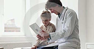 Pediatrician talks to little patient use tablet during clinic visit