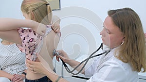 Pediatrician woman listening to heartbeat of girl using stethoscope in clinic.