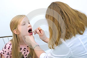 Pediatrician woman looking child girl sore throat using spatula and lantern.