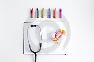 Pediatrics equipment with crayons, copybook white background top view space for text