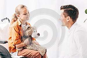 Pediatrist and kid with teddy bear on wheelchair