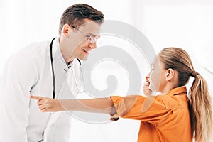 Pediatrist in white coat and child touching nose in clinic photo