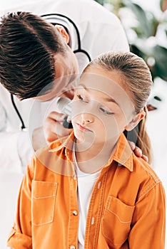 Pediatrist in white coat examining child with dermascope