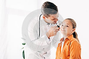 Pediatrist in white coat examining child with dermascope