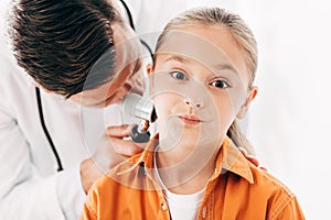 Pediatrist in white coat examining child with dermascope on white