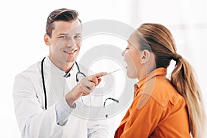 Pediatrist in white coat examining child with medical spatula