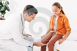 Pediatrist in white coat examining kid with reflex hammer