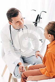 Pediatrist in white coat examining kid with reflex hammer