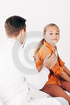 Pediatrist in white coat examining kid with stethoscope