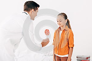 Pediatrist in white coat giving candy to child