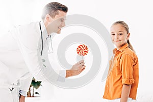 Pediatrist in white coat giving candy to child photo