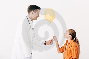 Pediatrist in white coat giving yellow balloon to kid photo