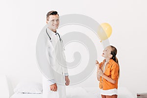 Pediatrist in white coat and happy child with balloon in clinic