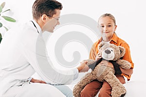 Pediatrist in white coat and kid with teddy bear in clinic photo