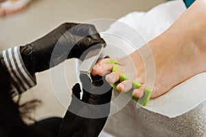 Chiropodist making black gloves making pedicure for her client photo