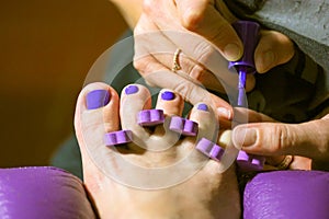 Pedicure master applies nail polish in beauty salon. Women& x27;s fingers toe divider