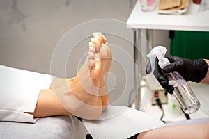 Pedicure master disinfects the feet of woman with the preparation decontamination in beauty salon.