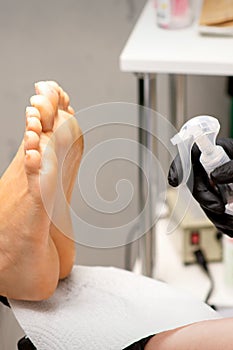 Pedicure master disinfects the feet of woman with the preparation decontamination in beauty salon.