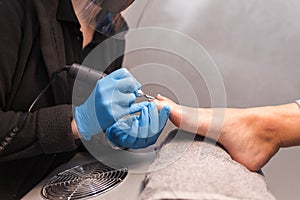 Pedicure master polishes nails with nail file drill before applying varnish side view