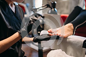 Pedicure master sprays foot nails of female client