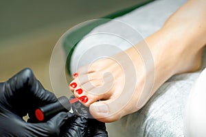 Pedicurist applying red nail polish