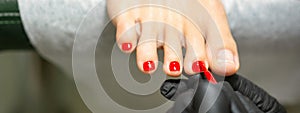 Pedicurist applying red nail polish to the female toenails in a beauty salon.