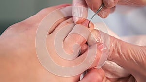 Pedicurist is cleaning nails from dry skin and dirt on toes using metal stick.