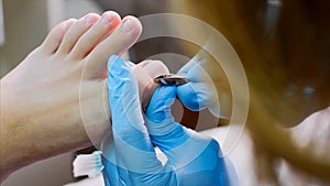 Pedicurist cuts cuticle on toe with nail tongs makes pedicure in beauty salon.