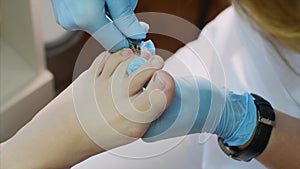 Pedicurist cuts cuticle on toe with nail tongs makes pedicure in beauty salon.