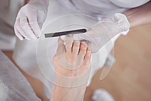 Pedicurist doing professional medical pedicure procedure in beauty salon using nail file. Foot treatment in SPA salon. Podiatry