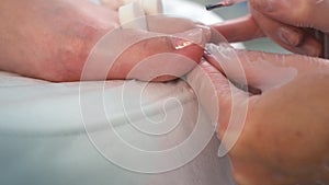 Pedicurist master is applying soft pink gel shellac on woman's toes, closeup.