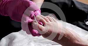 Pedicurist master in pink gloves is cuts the cuticle and shellac toe nails in the pedicure salon using drill.  Professional pedicu