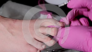 Pedicurist master in pink gloves is cuts the cuticle and shellac toe nails in the pedicure salon using drill.  Professional pedicu