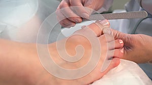 Pedicurist master woman is filing nails on toes using nail file, hands closeup.