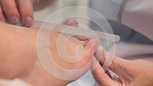 Pedicurist master woman is filing nails on toes using nail file, hands closeup.