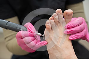 A pedicurist treats the toes of a client using a machine with an abrasive disc in a beauty salon.