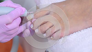 Pedicurist woman removes cuticle from client`s toes using electric nail machine.