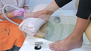 Pedicurist woman removes cuticle from client`s toes using electric nail machine.