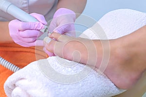 Pedicurist woman removes cuticle from client`s toes using electric nail machine.