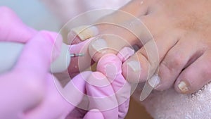 Pedicurist woman removes cuticle from client`s toes using electric nail machine.