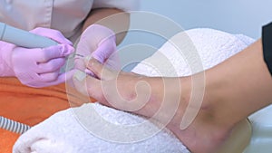 Pedicurist woman removes cuticle from client`s toes using electric nail machine.